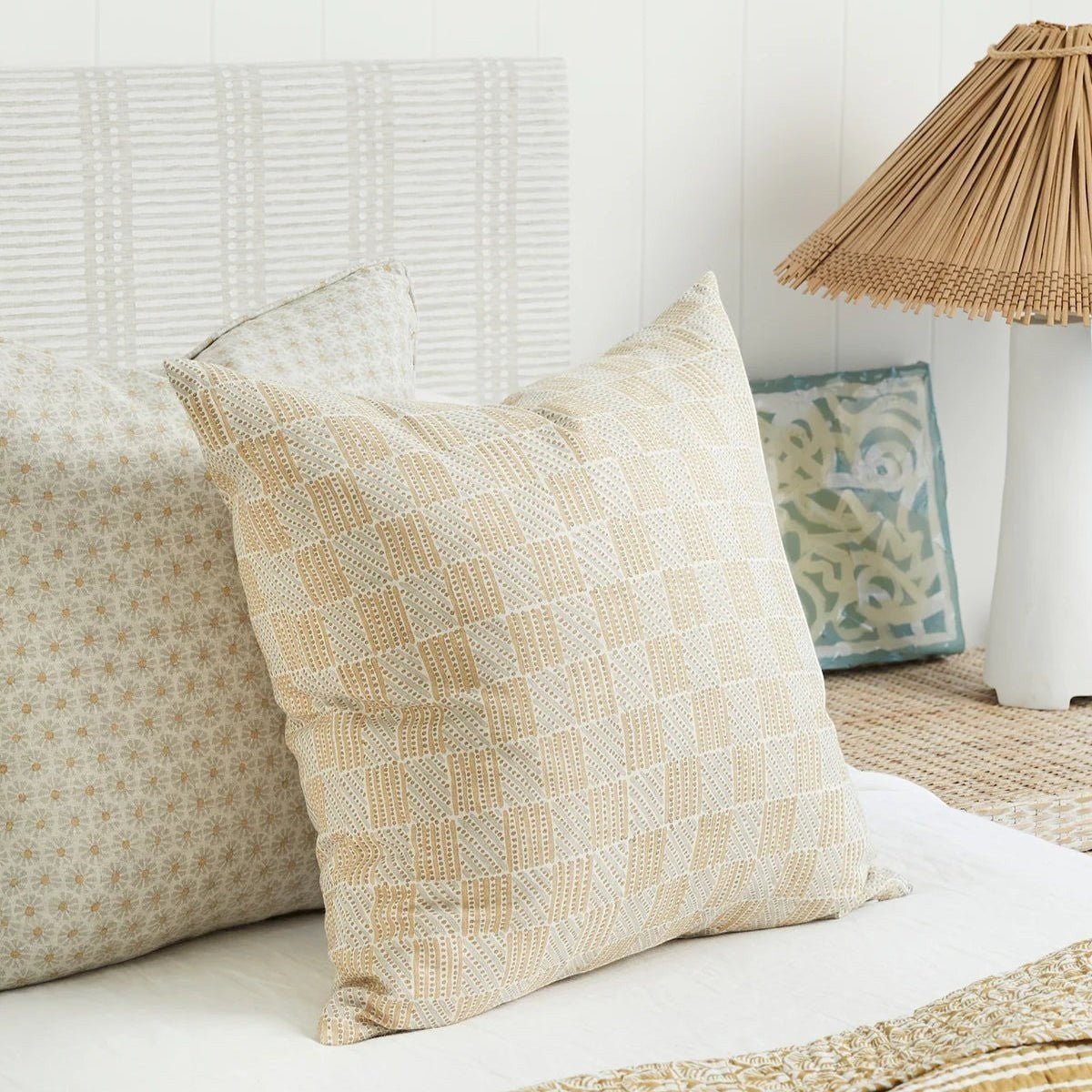 Walter G Kumasi Elm linen pillow with hand block printed grid pattern in neutral tones on a bed.