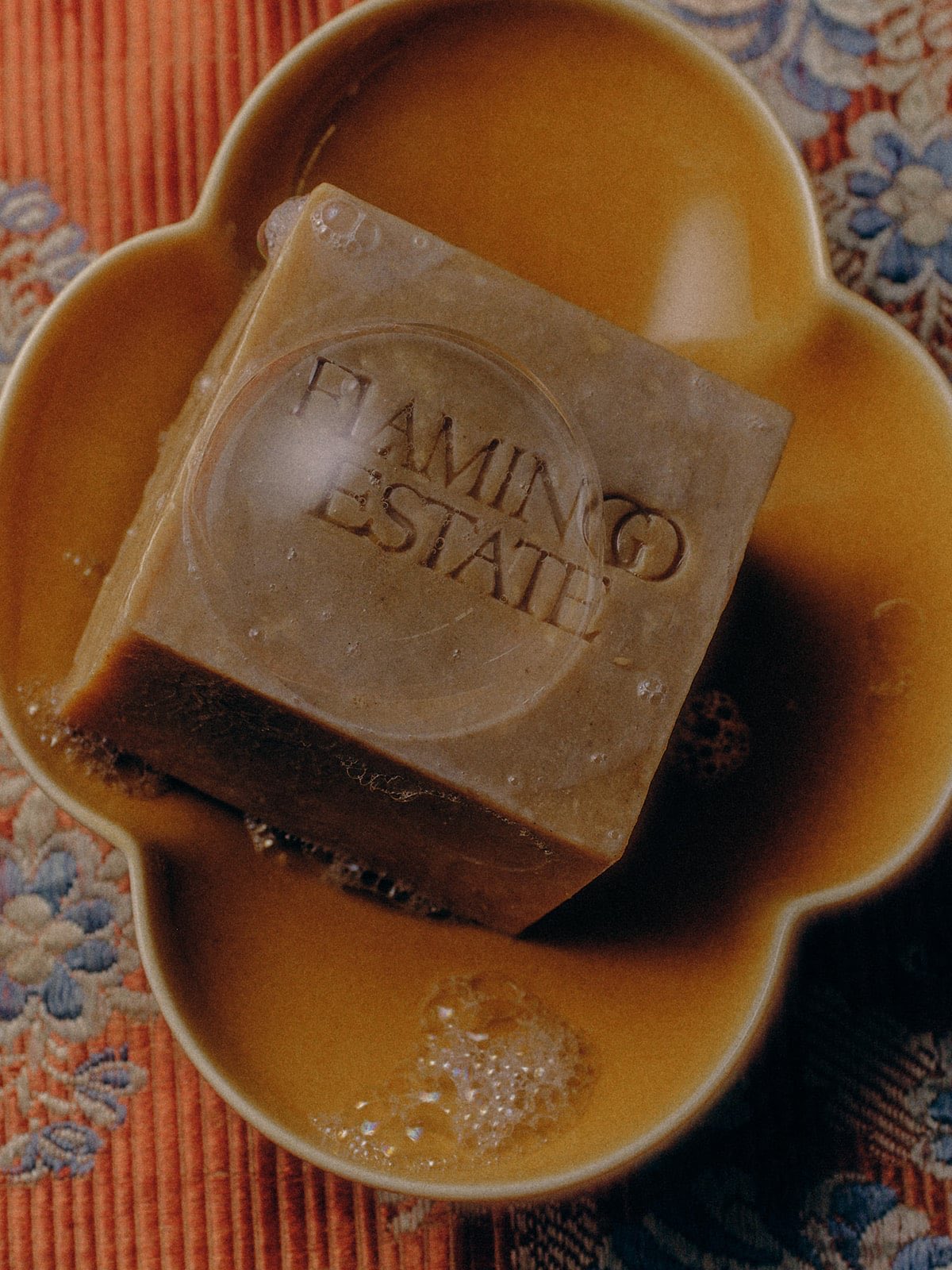 Flamingo Estate Manuka Honey Soap Brick resting beside a jar of golden manuka honey and fresh flowers, styled on a warm neutral surface.