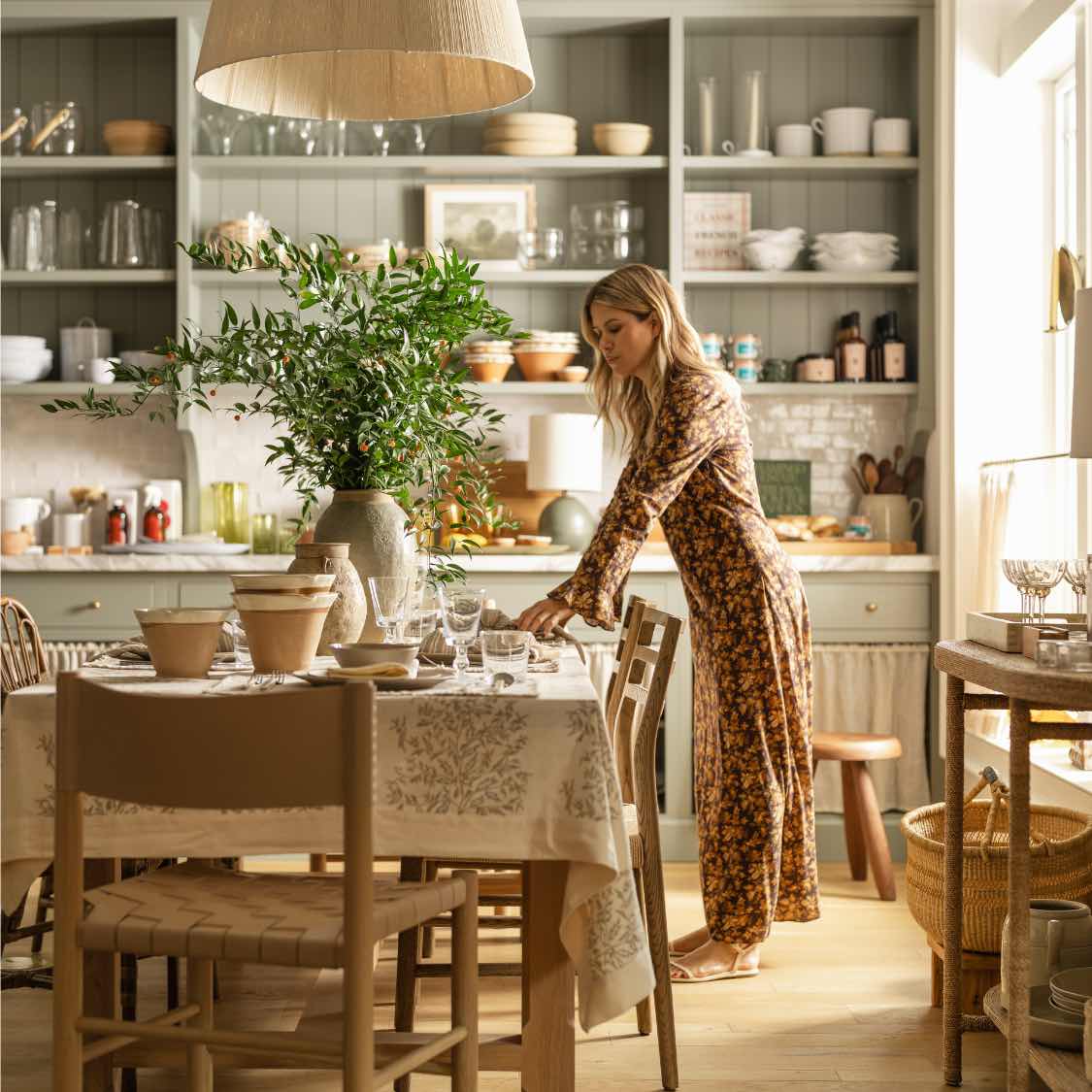 Monique Miller of Calimia Home sets a dining table in a sunlit sage-green kitchen.