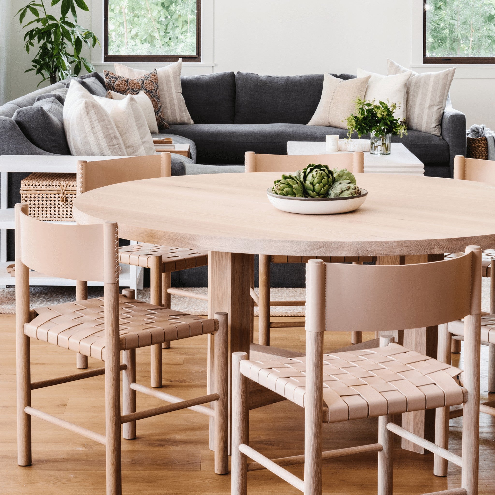 Valencia X Dining Table in natural oak by Grove & Anchor, styled with woven-seat dining chairs beside a living area, exclusive to Calimia Home