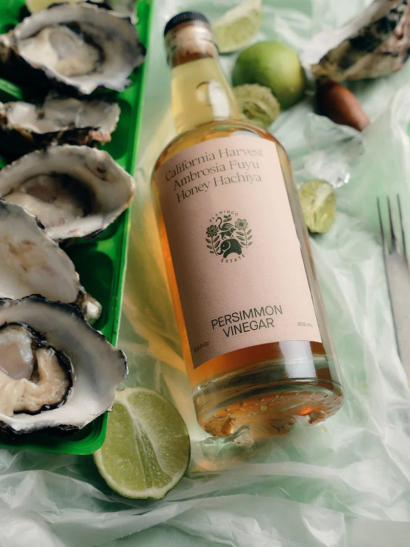 Flamingo Estate Persimmon Vinegar perches on tissue paper next to a tray of freshly shucked oysters on the half shell with lime wedges.