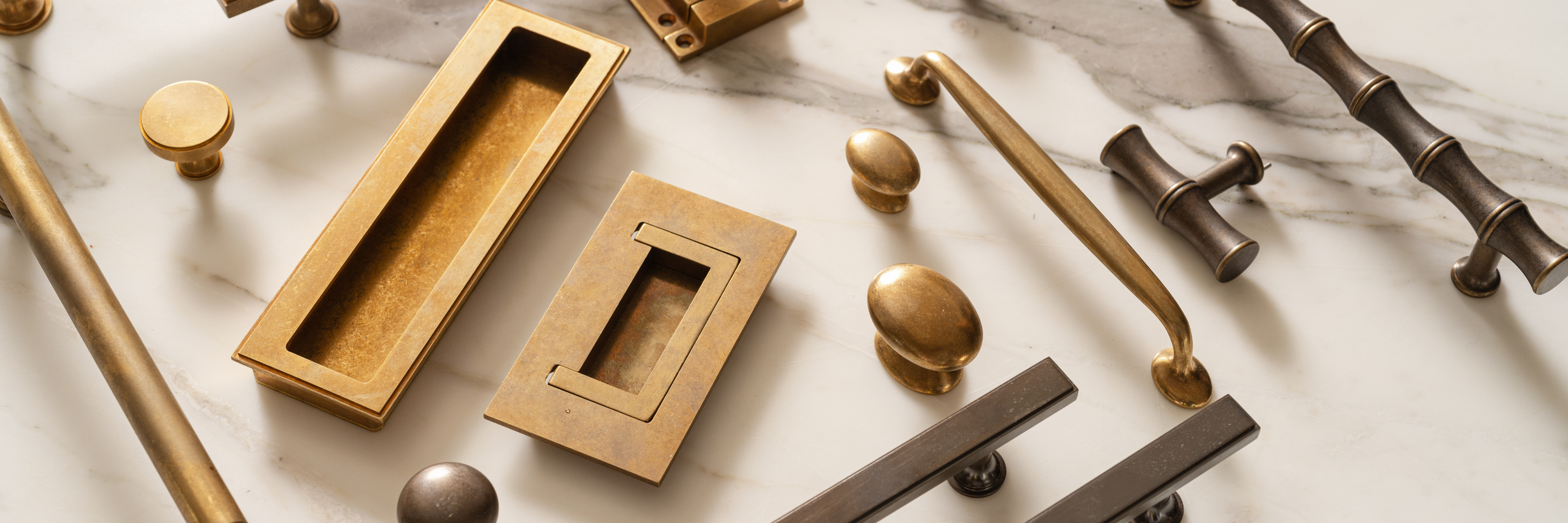 Mixed brass and bronze cabinet knobs and pulls styled on a marble surface for hardware selection