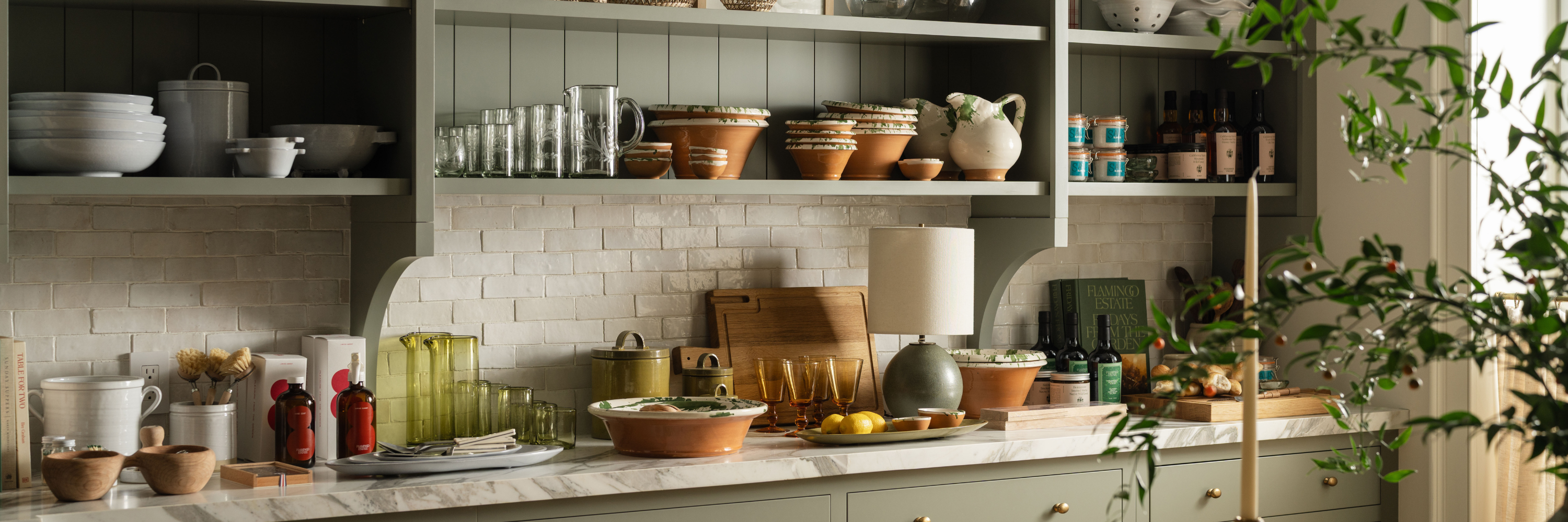 Ceramic bowls, glassware, terracotta serveware, and pantry staples styled on open kitchen shelves and marble countertop