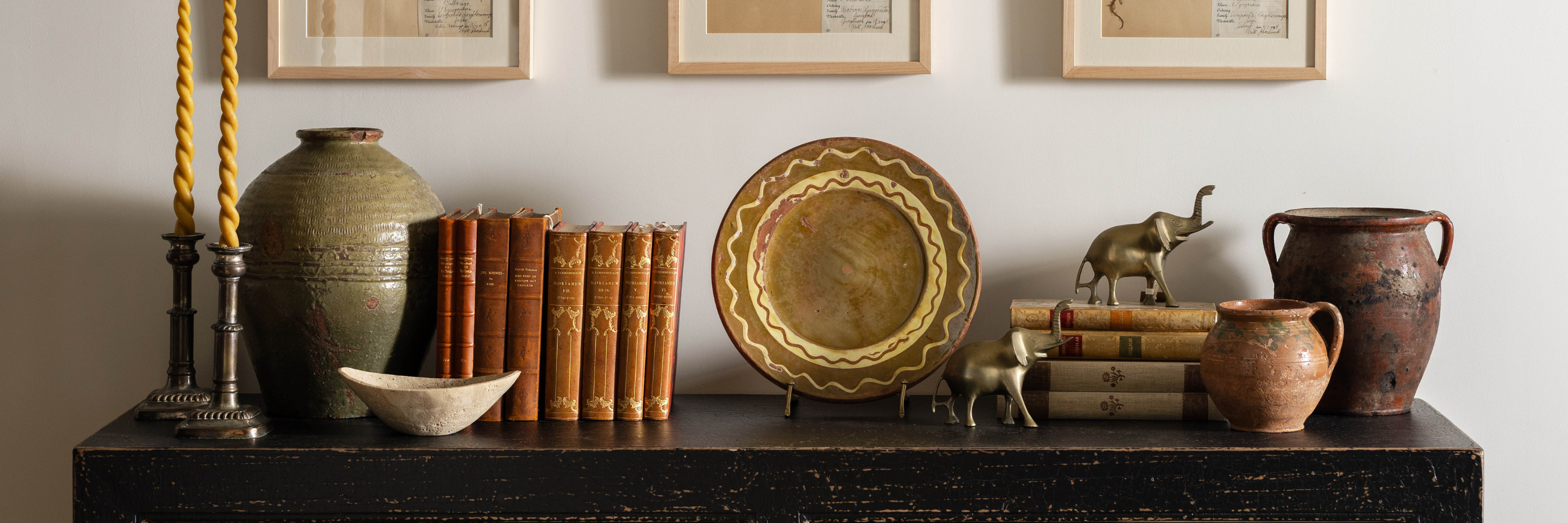 Collected vintage books, pottery, brass decor pieces, and candlesticks styled on a dark console table