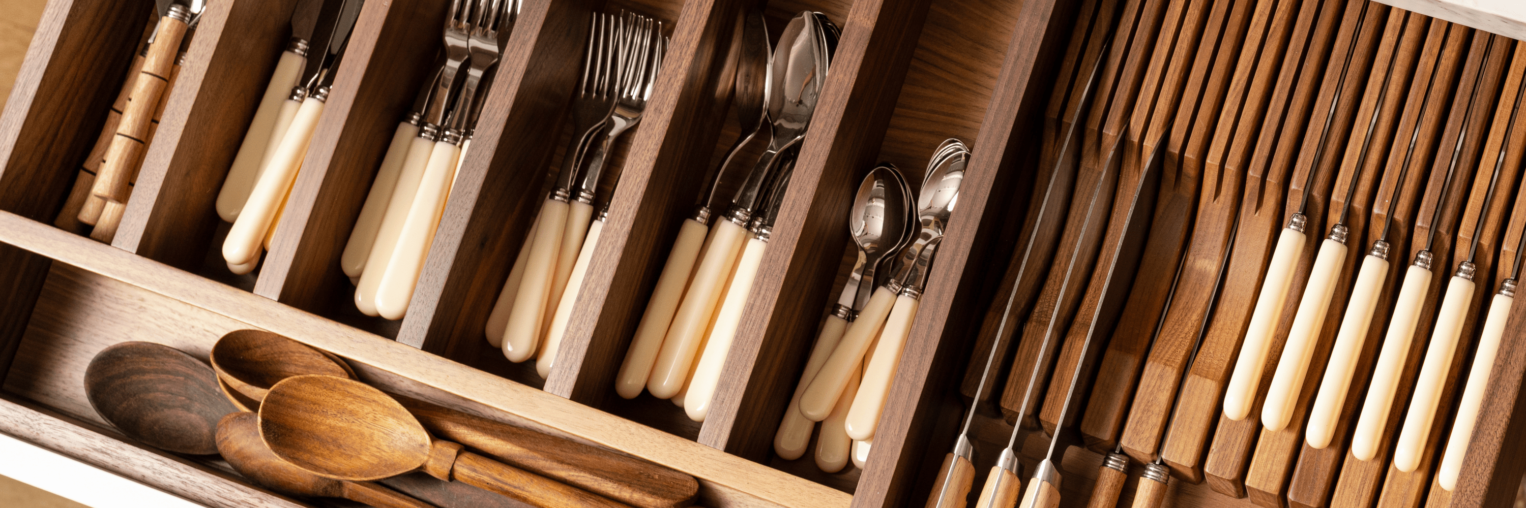 Round wooden dining table set with neutral dinnerware, linen napkins, and wildflowers in a glass pitcher. Soft light filters through linen curtains behind a cushioned bench at Calimia Home Shop.
