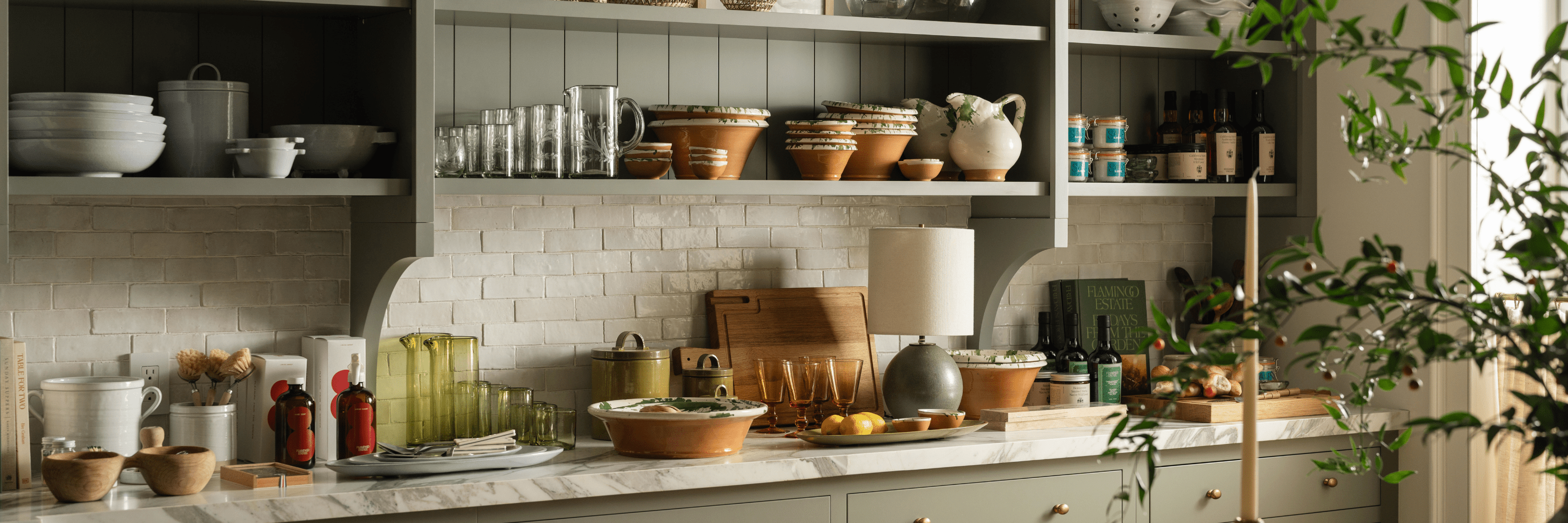 Ceramic bowls, glassware, terracotta serveware, and pantry staples styled on open kitchen shelves and marble countertop