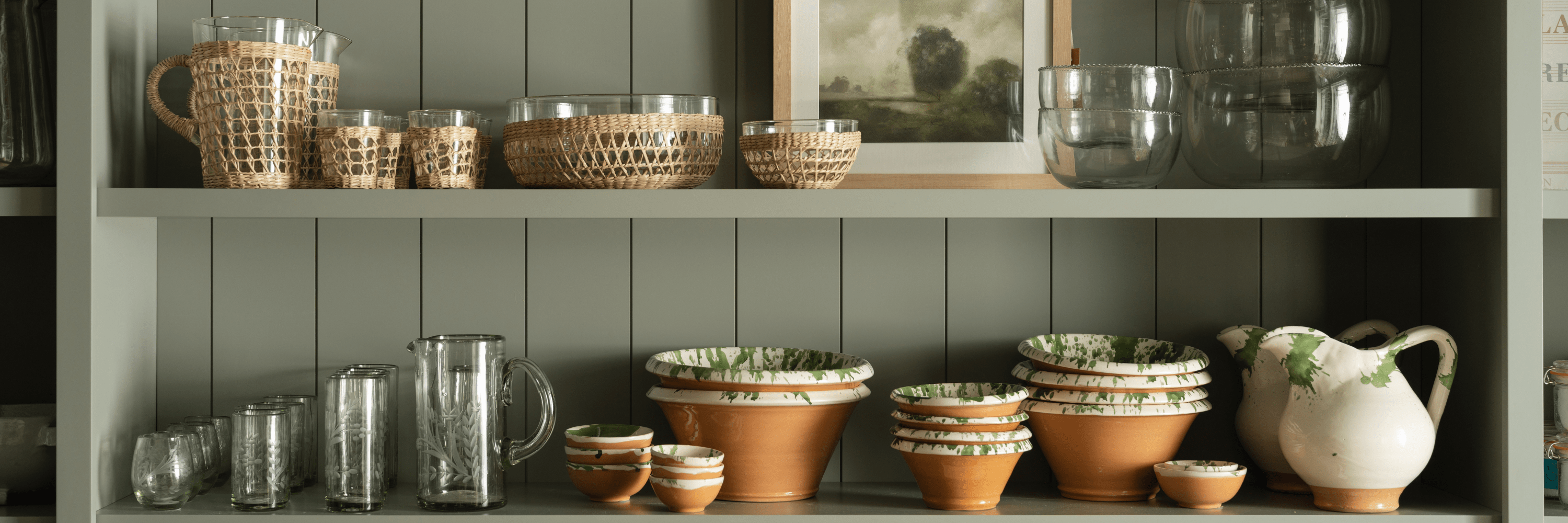 Woven baskets, glass pitchers, and splatter-paint ceramic bowls and jugs arranged on open shelves