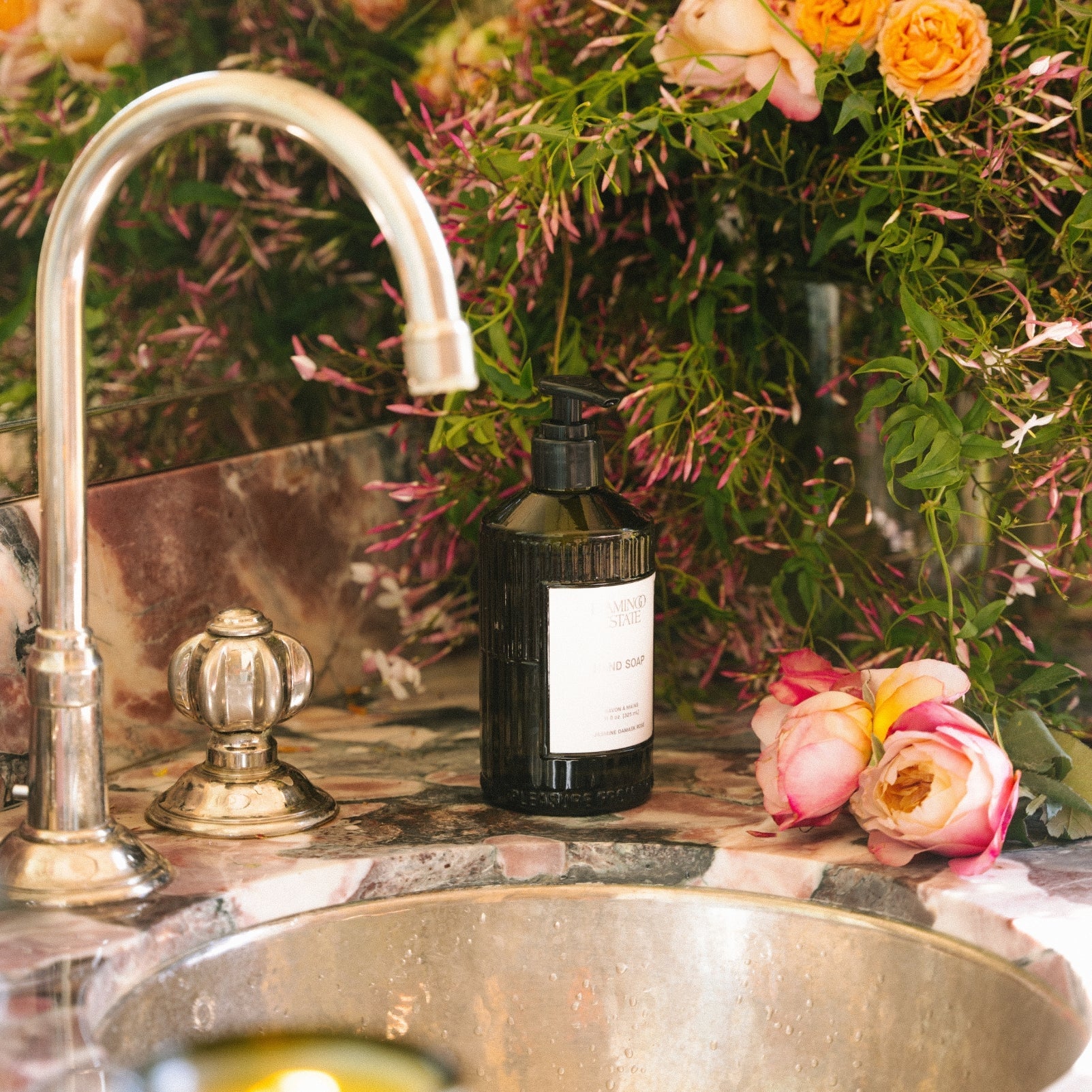 Flamingo Estate Jasmine Damask Rose Hand Soap glass bottle styled on a soft neutral surface, the fluted forest-green vessel catching warm light.