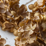 Artificial hydrangea stem with abundant clusters of small flowers in warm sunset tones, single stem detail