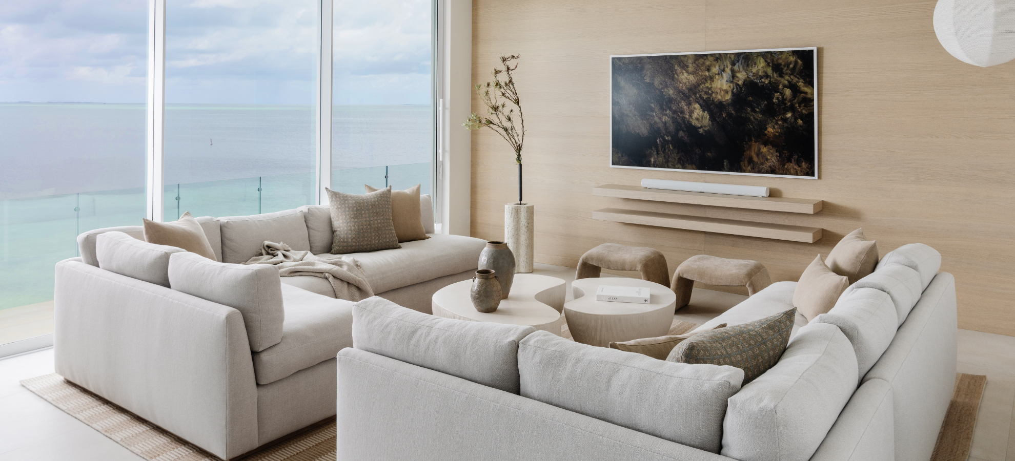 Modern living room with white sofas, a TV, and large windows overlooking water.