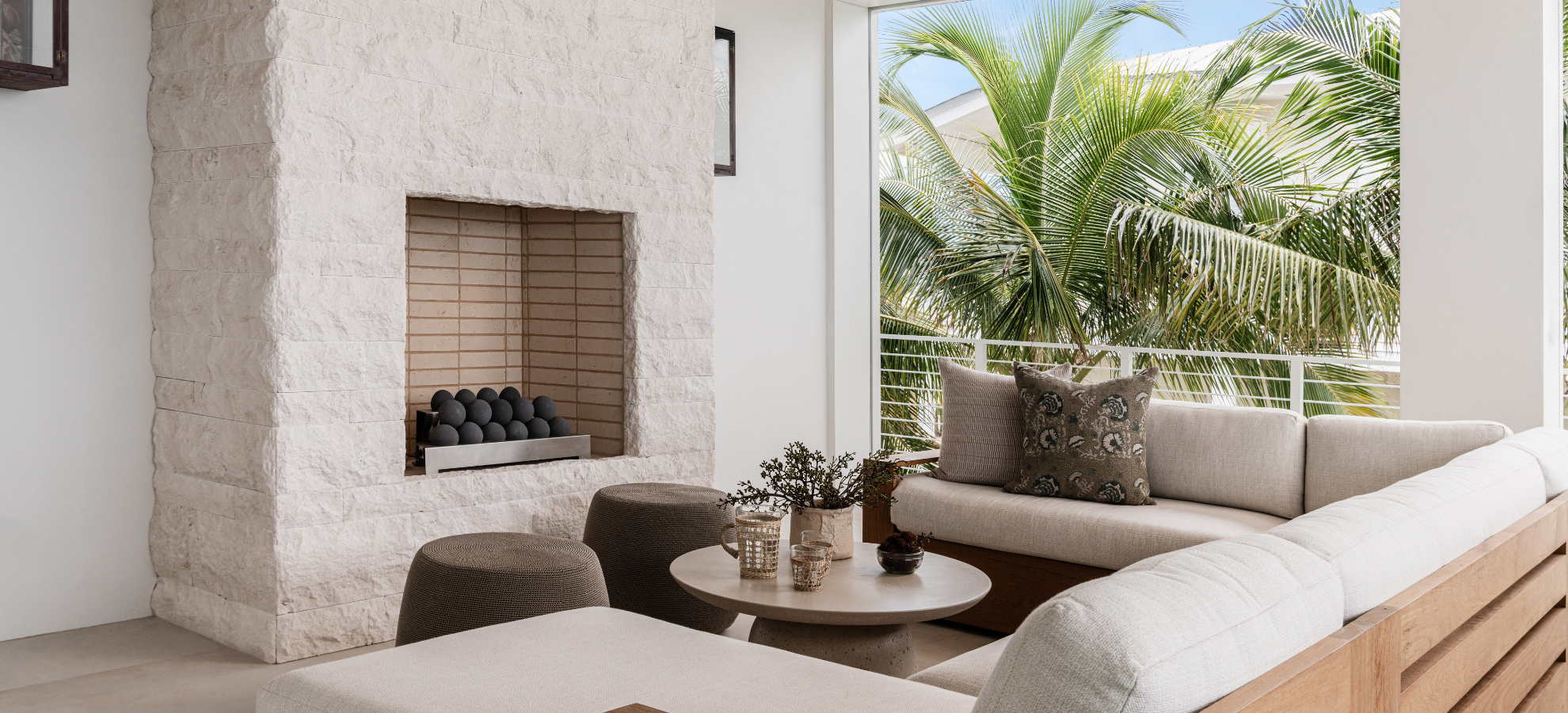 Modern living room with a fireplace, sofa, and outdoor view of palm trees.