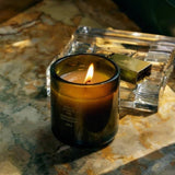 Flamingo Estate Adriatic Muscatel Sage candle in a fluted forest-green glass vessel with soy wax, lit on a stone surface.
