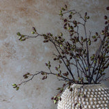Artificial Barberry stems by Abigail Ahern arranged in a textured cream vase against a plaster wall