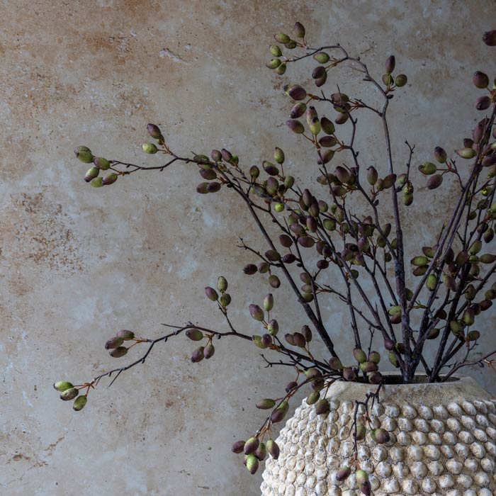 Artificial Barberry stems by Abigail Ahern arranged in a textured cream vase against a plaster wall