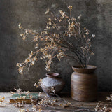 Artificial Hibernal Blossom Soft Blush stems by Abigail Ahern in a wooden vessel against a dark plaster wall