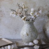 Artificial Magnolia stems by Abigail Ahern arranged in a speckled stone vase against a plaster wall