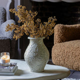 Artificial Sedge Winter Saffron by Abigail Ahern in a textured white vase beside a boucle chair