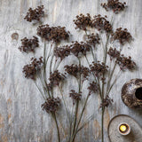 Artificial Woodland Yarrow by Abigail Ahern laid flat on a weathered wood surface beside a candle