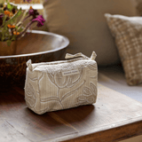 Astrid quilted toiletry bag in Sand on a wooden table beside a bowl and linen cushions