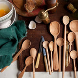 Sir Madam set of 13 hand-carved beechwood spoons in assorted sizes and shapes on a rustic wooden kitchen surface.