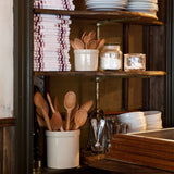 Sir Madam set of thirteen hand-carved beechwood spoons in a white ceramic crock on a kitchen shelf.