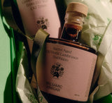 The Flamingo Estate Balsamic Vinegar bottle nests in green tissue and ribbon beside a Heritage olive oil, ready as a gift from Calimia Home Shop.
