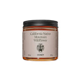 A clear glass jar of Flamingo Estate California Native Mountain Wildflower Honey with a cream label, on a white background.