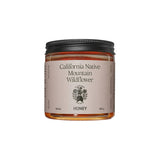 A clear glass jar of Flamingo Estate California Native Mountain Wildflower Honey with a cream label, on a white background.