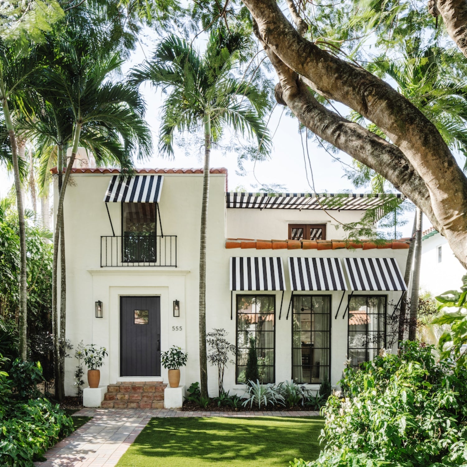 White Mediterranean home with striped awnings and palm trees, a Calimia Home design project