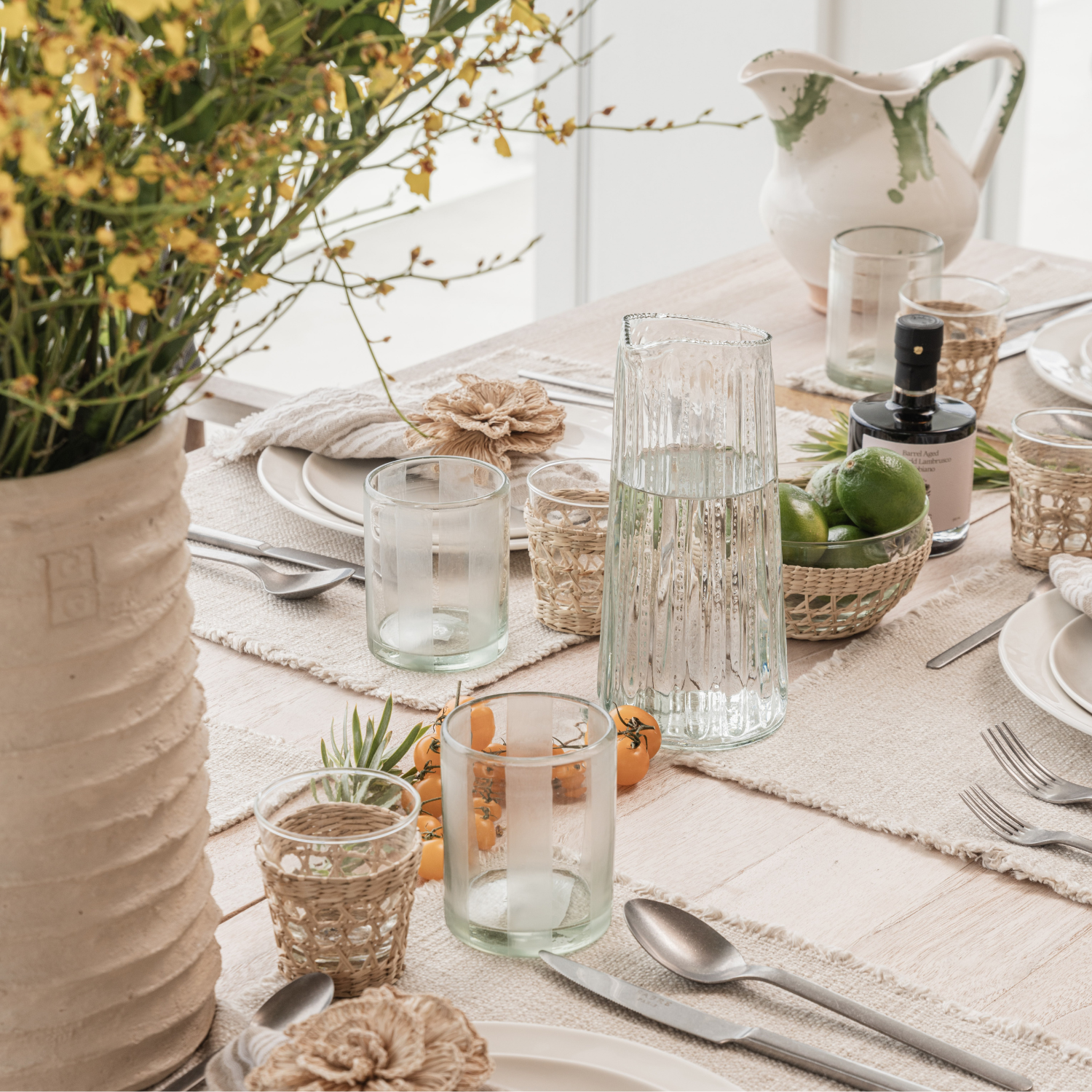 Styled dining tablescape with recycled glassware, woven crochet cup sleeves, linen placemats, and fresh florals
