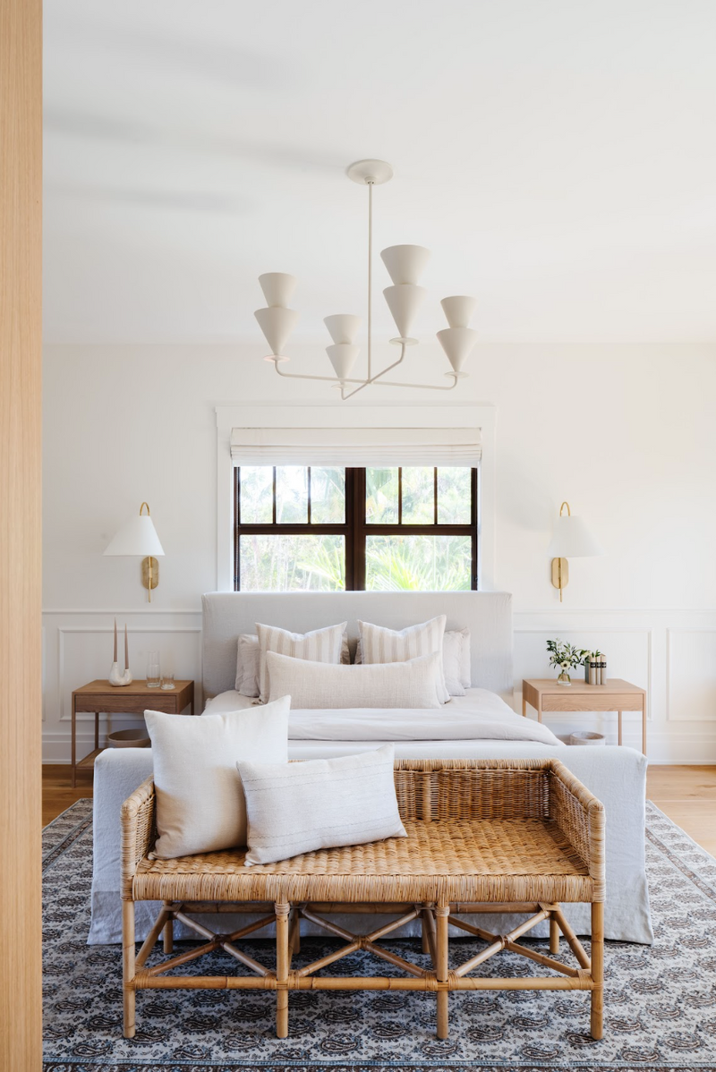 Airy bedroom with rattan bench, plaster chandelier, and blue patterned rug in the Coral Way Craftsman home