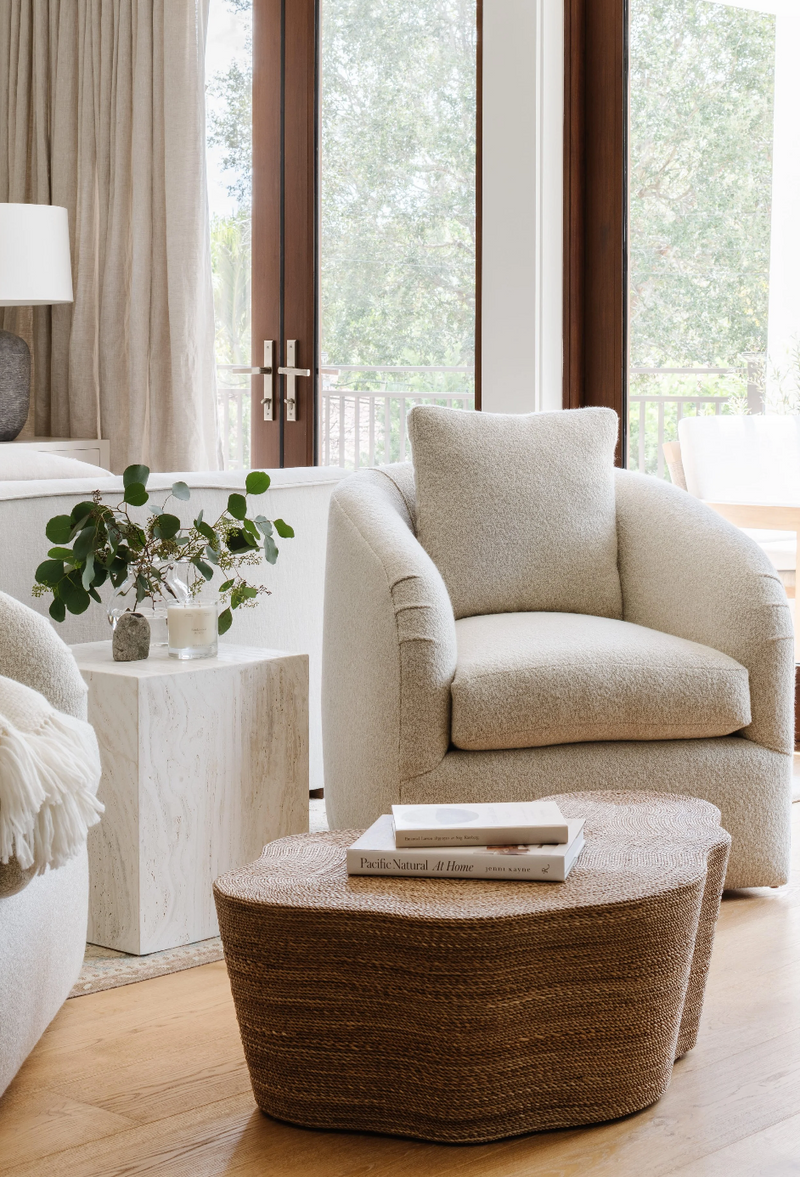 Cream boucle armchair and sculptural woven coffee table beside floor-to-ceiling glass doors