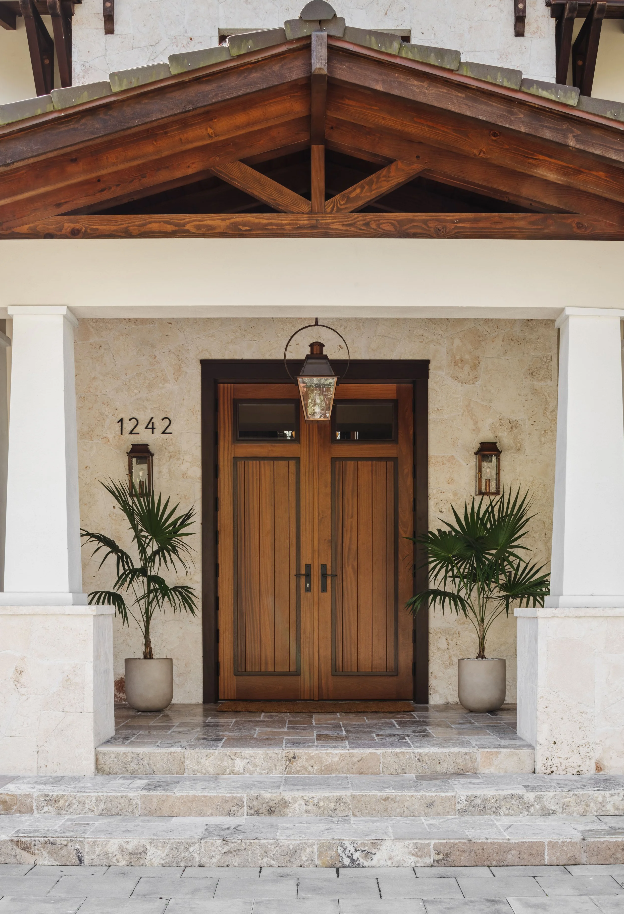 Craftsman double front doors framed by a timber gable and potted palms at the Coral Way Craftsman home