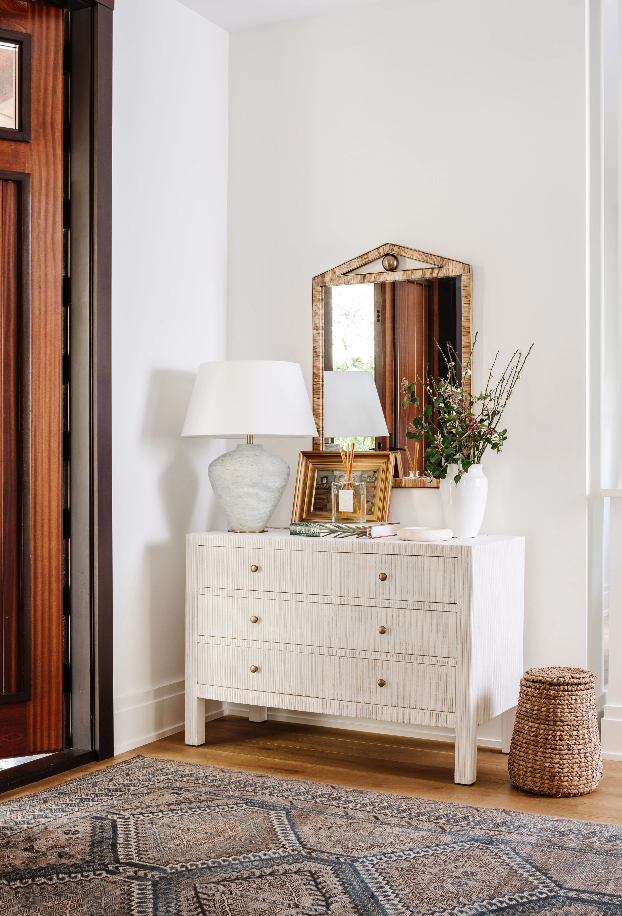 Entry vignette with carved white dresser, antique brass mirror, and layered vintage rug