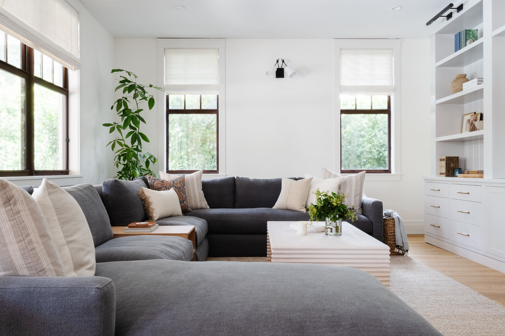 Bright family room with charcoal sectional and built-in shelving, designed by Calimia Home