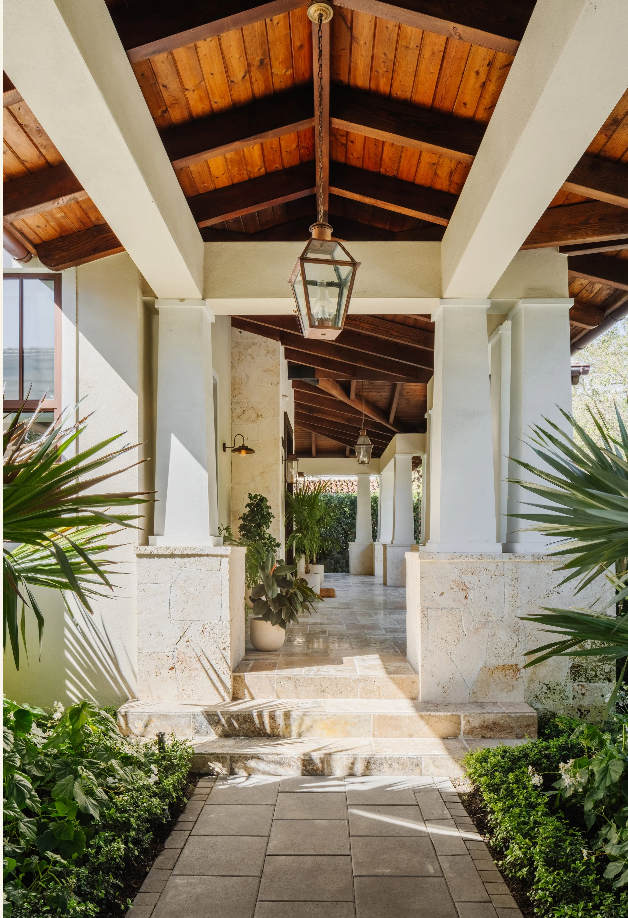 Covered front walkway with stained wood ceiling, lantern pendants, and coral stone columns