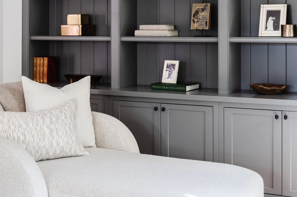 Gray-painted library built-ins styled with framed photos behind a white boucle chaise