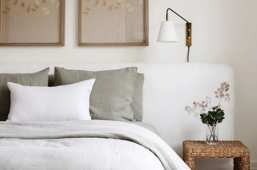 Guest bedroom detail with linen bedding, brass sconce, and earthy botanical artwork
