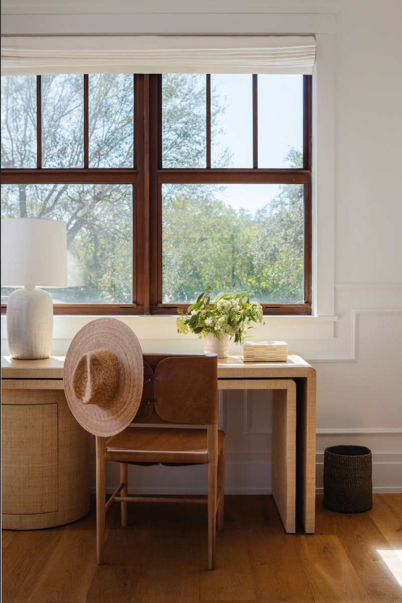 Sunlit home office nook with oak nesting desks, cane chair, and straw hat by the window