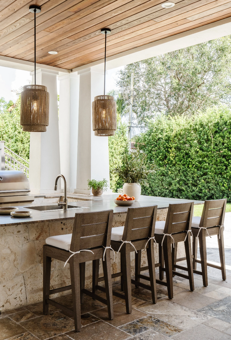 Outdoor kitchen with coral stone island, rattan pendants, and teak barstools at the Coral Way Craftsman project, Miami