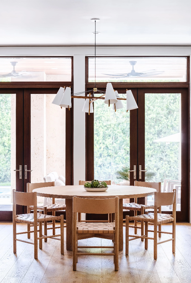 Oval dining table with spindle chairs beneath a modern chandelier and dark-framed French doors