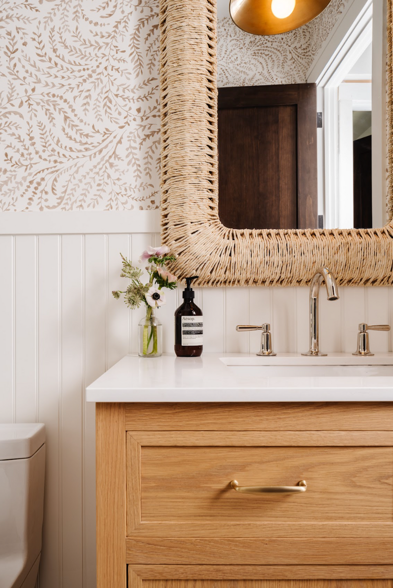 Powder bath with woven rattan mirror, fern wallpaper, and white oak vanity