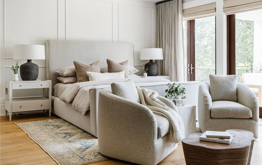 Serene primary bedroom layered in warm neutrals with upholstered bed and a pair of armchairs