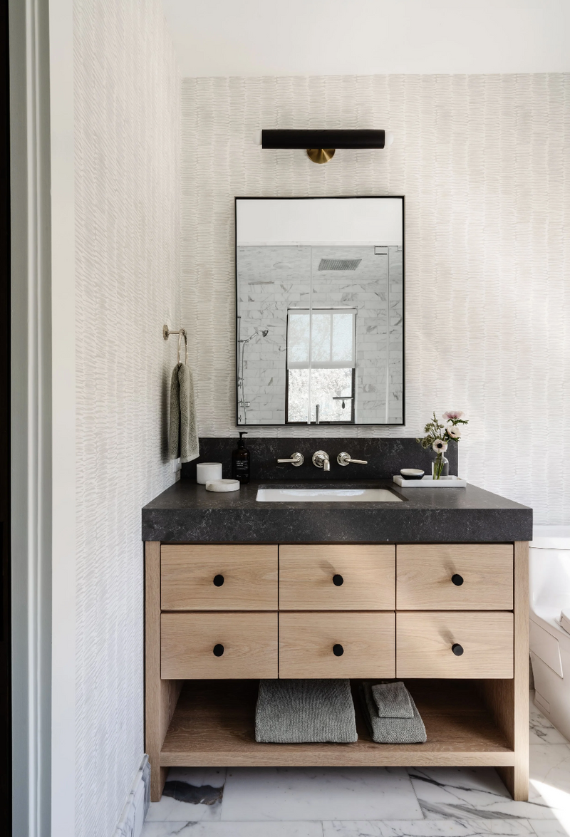 Bathroom vanity in white oak with honed black stone counter and textured wallpaper