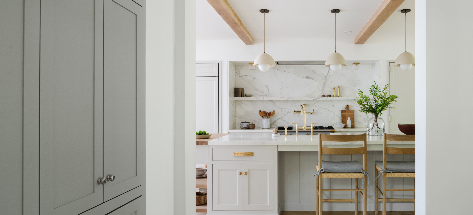 Custom kitchen cabinetry by Calimia Home with marble backsplash, brass pendants, and woven counter stools