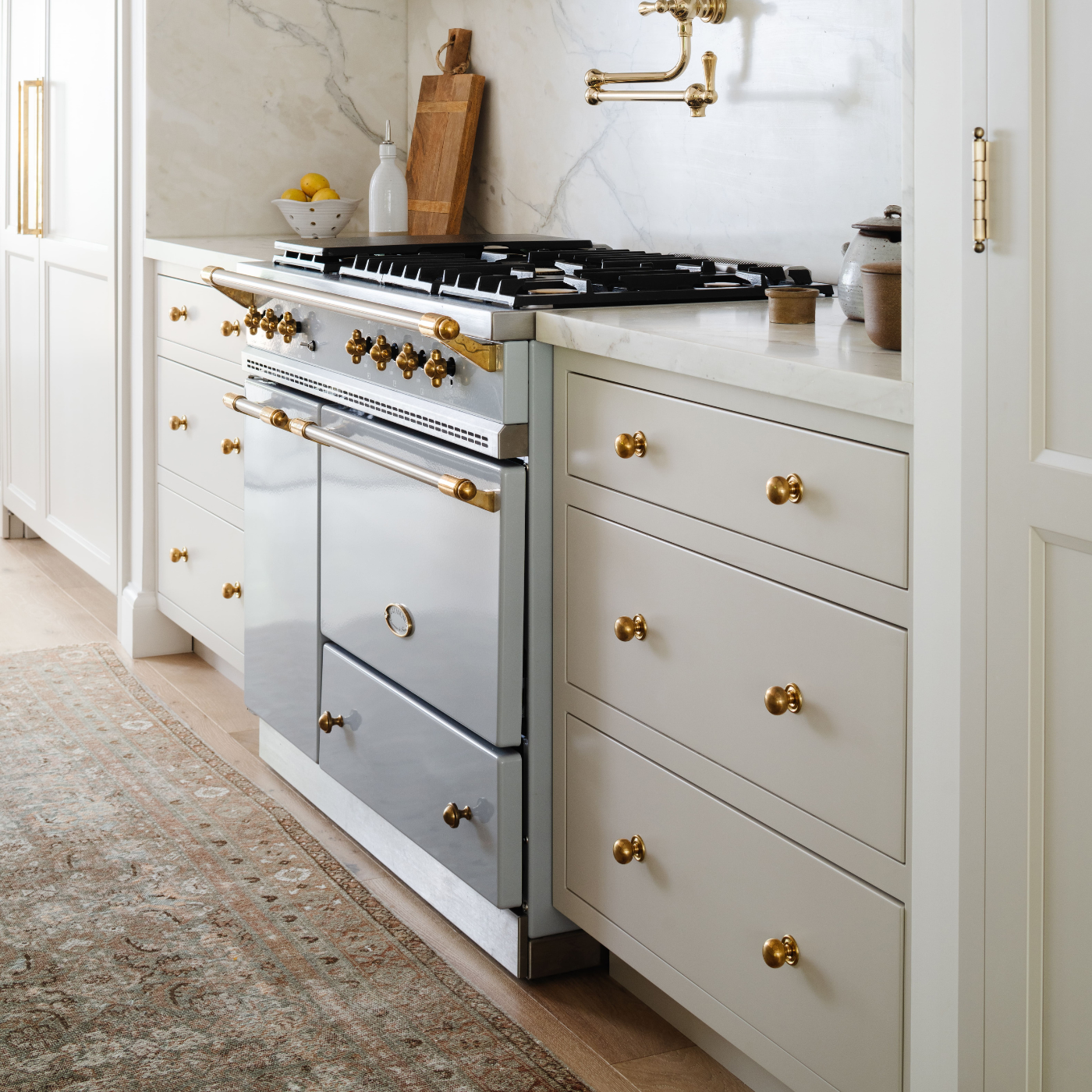 Cream custom cabinetry with brass hardware surrounding a French range, installed by Calimia Home