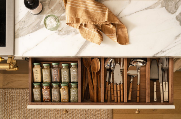 Open kitchen drawer with walnut spice and utensil inserts under a marble countertop