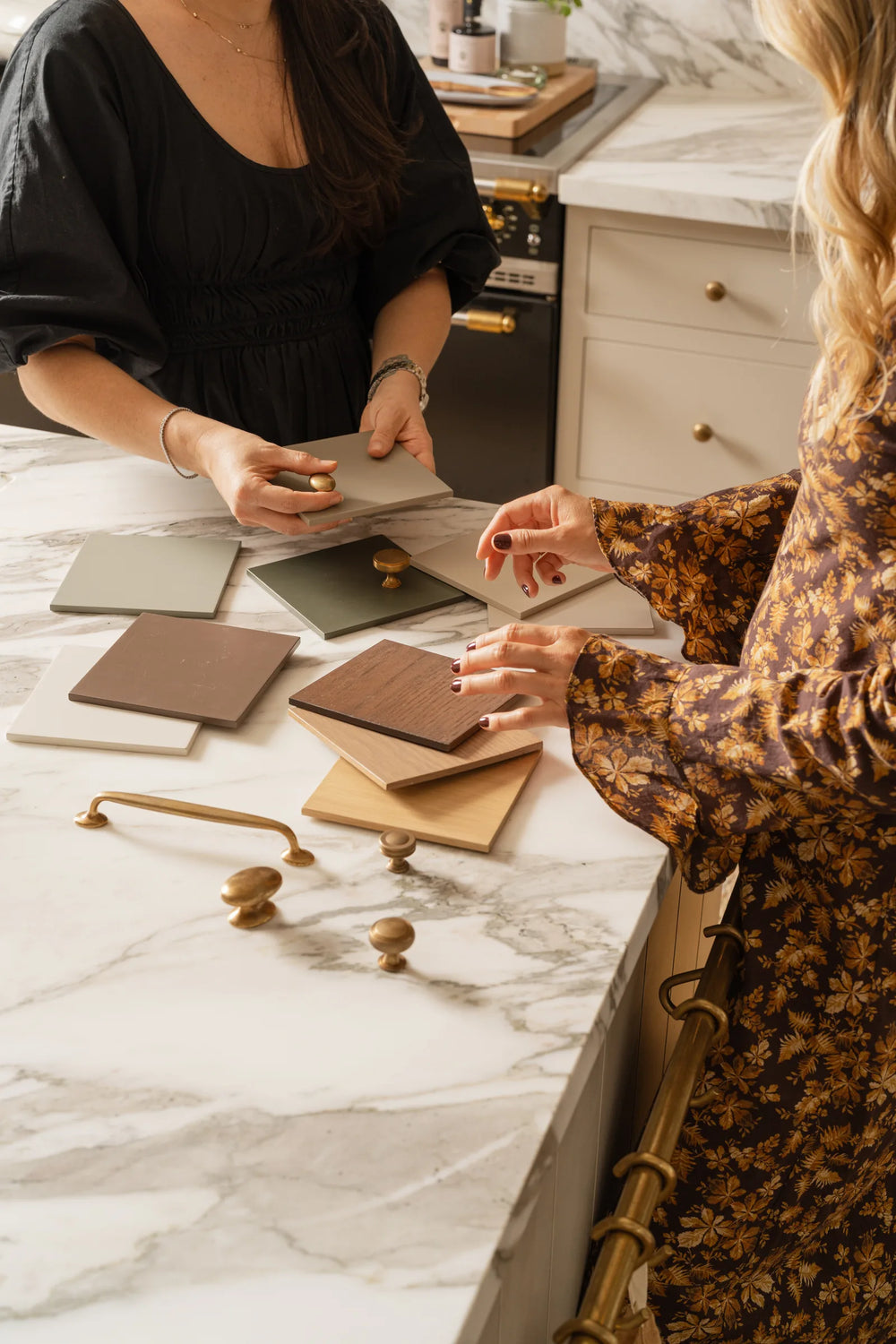 Designers comparing painted cabinet finish samples and brass hardware on a marble island
