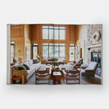 Calimia Home Everybody Loves Stripes book open to a spread showing a wood-panelled living room with a stone fireplace.
