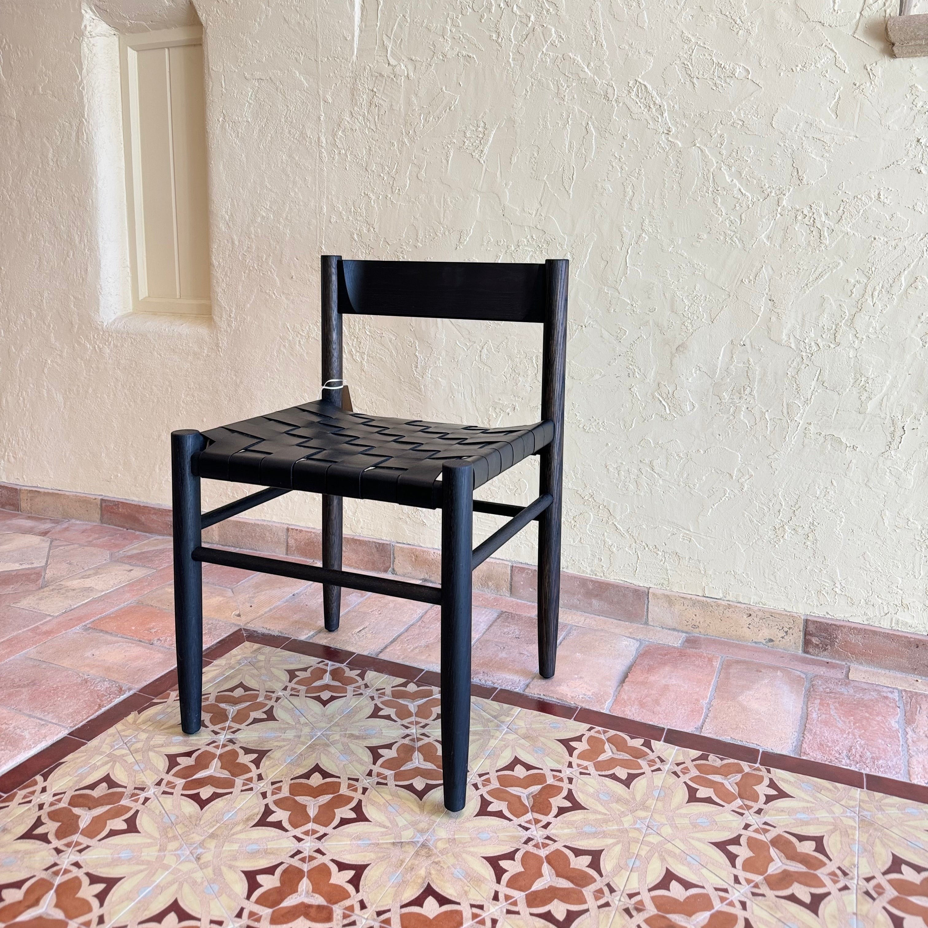 Calimia Home Gaon chair featuring a black oak frame and a woven black leather seat on a tiled floor.